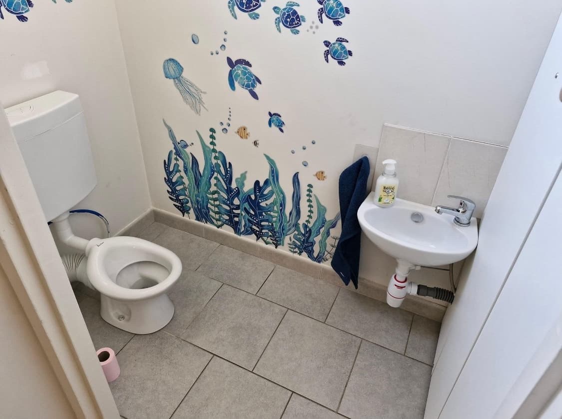 Un petit coin toilettes adapté aux enfants avec un lavabo bas et des stickers muraux sur le thème de la mer.