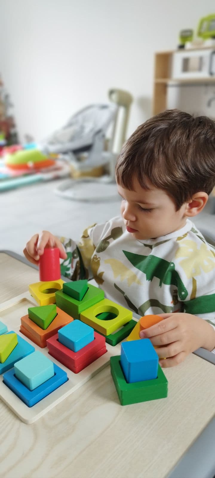 Un enfant concentré manipule des formes géométriques en bois colorées sur un plateau de jeu, développant sa motricité fine.