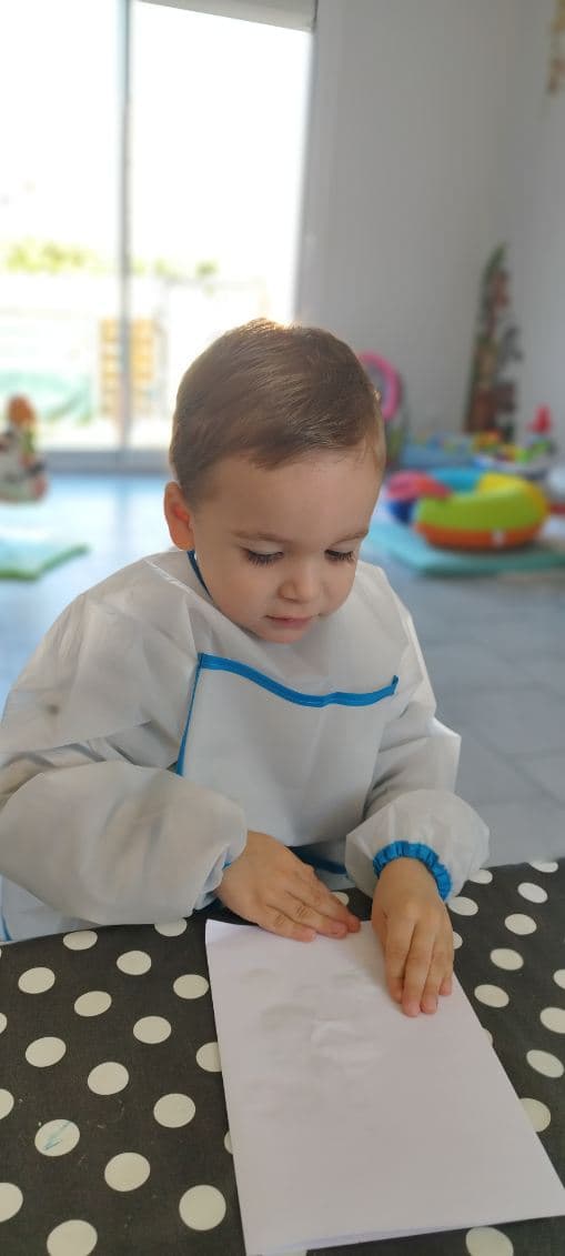 Un enfant portant un tablier de protection est assis devant une feuille blanche, prêt pour une activité créative.