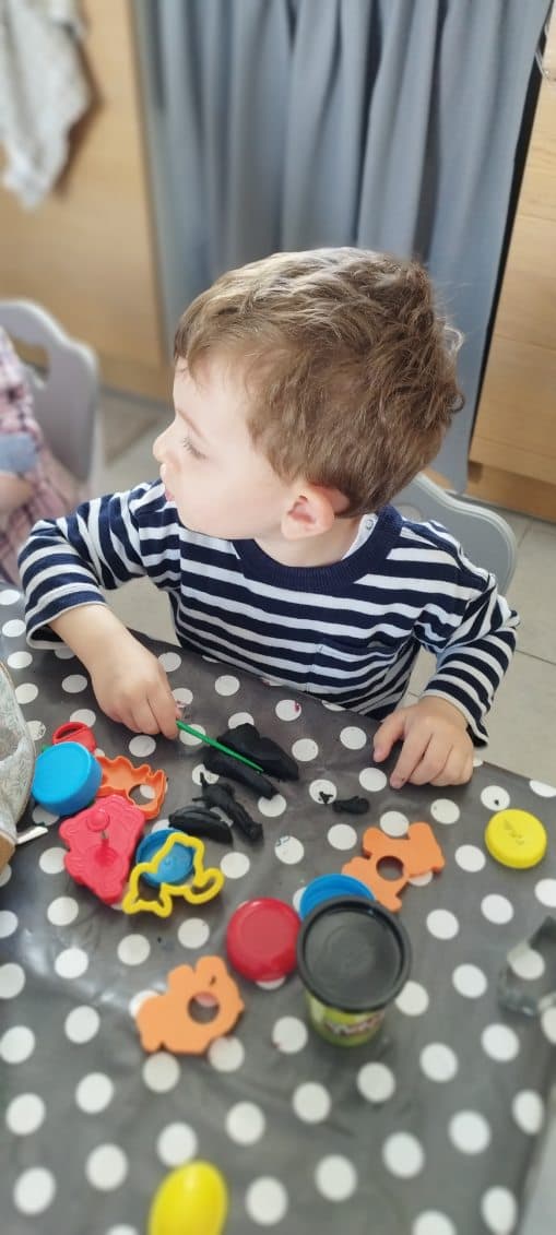 Un enfant est assis à une table à pois et joue avec de la pâte à modeler et des emporte-pièces colorés, concentré sur son activité créative.