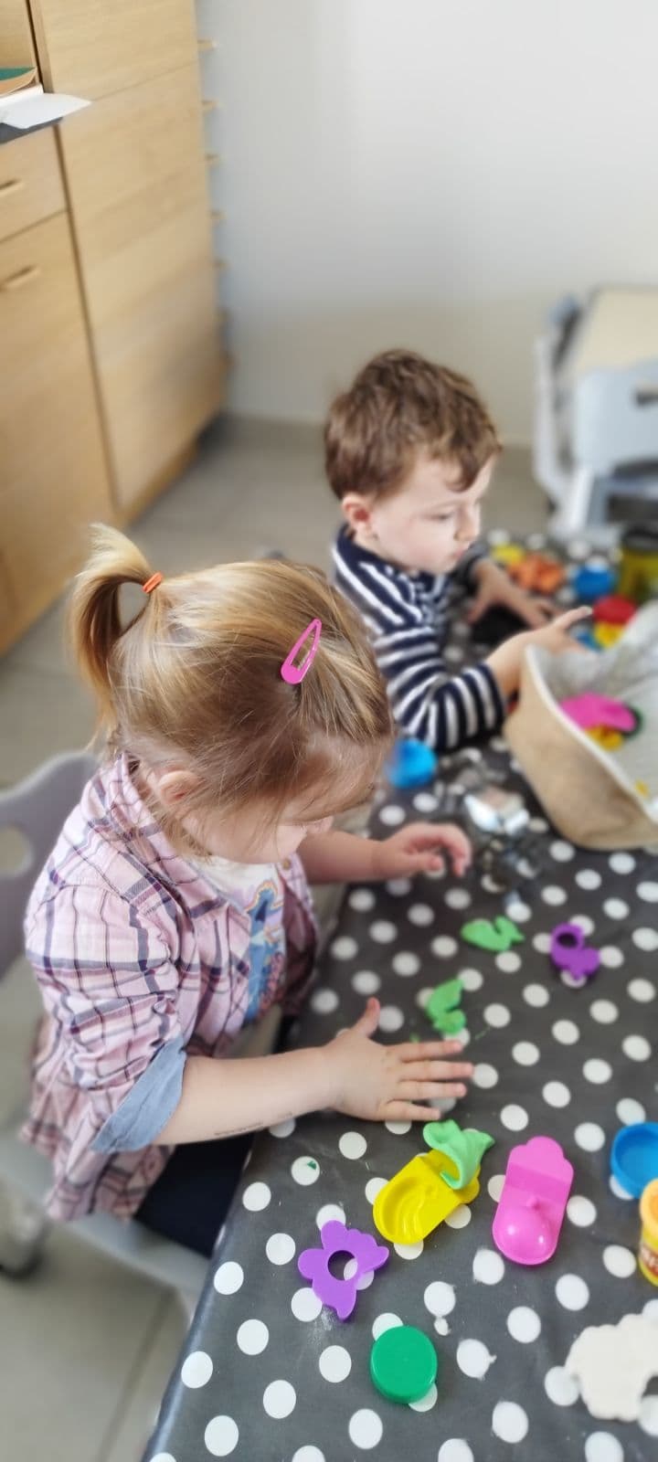 Des enfants sont assis à une table à pois et s'amusent avec de la pâte à modeler colorée et des petits moules en plastique.
