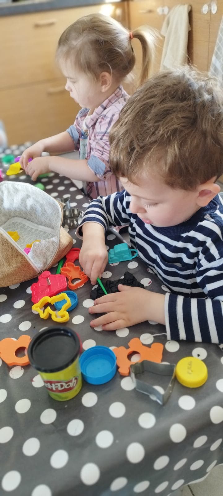 Des enfants sont assis autour d'une table à pois, concentrés sur une activité de modelage avec de la pâte à modeler et des emporte-pièces colorés.