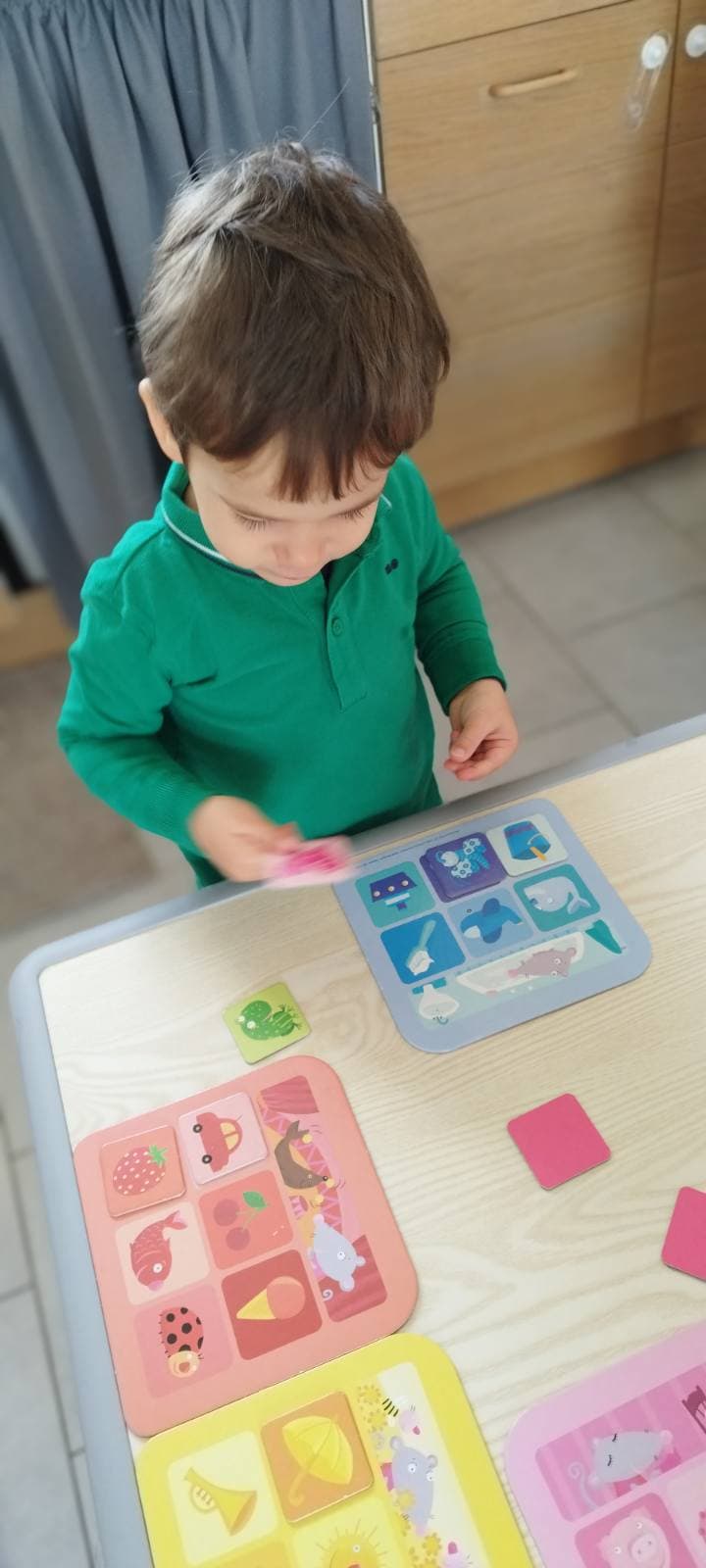 Un enfant concentré joue avec des cartes illustrées colorées sur une table, en train d'associer des images dans un jeu éducatif ludique.
