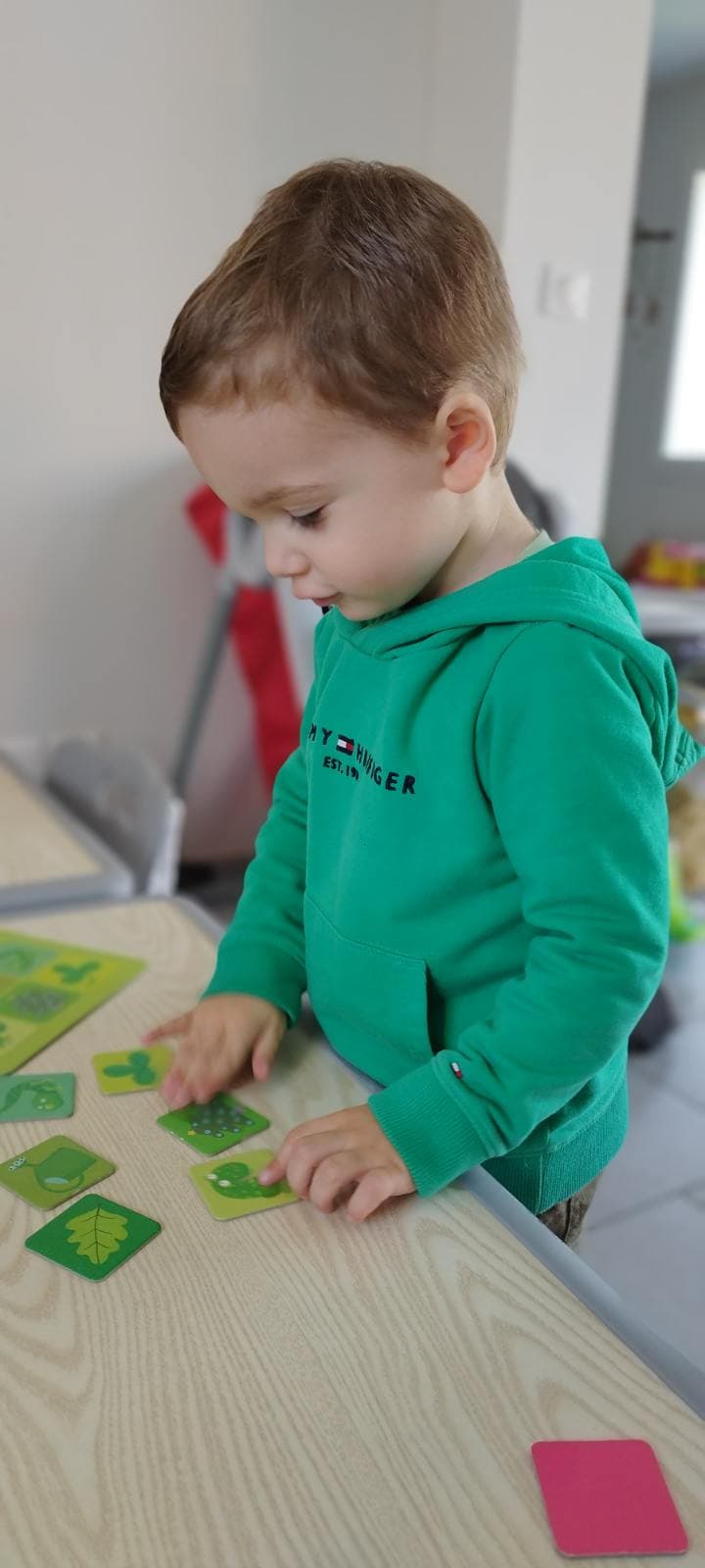 Un enfant concentré manipule des petites cartes de jeu vertes illustrées sur une table en bois.