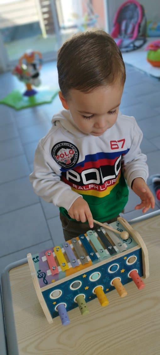 Un enfant joue avec un xylophone en bois coloré, explorant les sons et les notes avec une petite baguette.