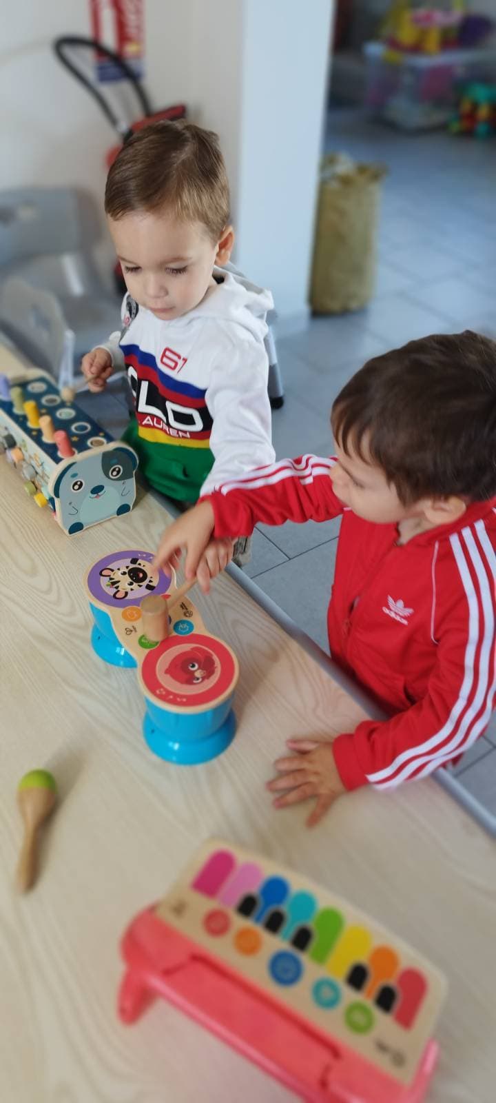 Deux enfants jouent joyeusement avec des instruments de musique en bois colorés sur une table claire, explorant les sons et les rythmes ensemble.