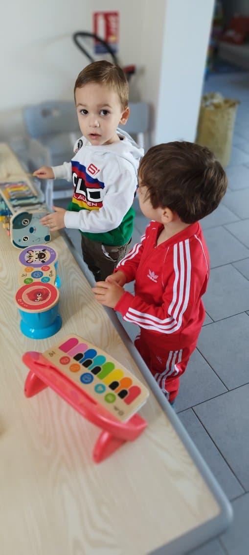 Deux enfants jouent avec des instruments de musique colorés posés sur une table en bois dans une salle de jeux lumineuse.
